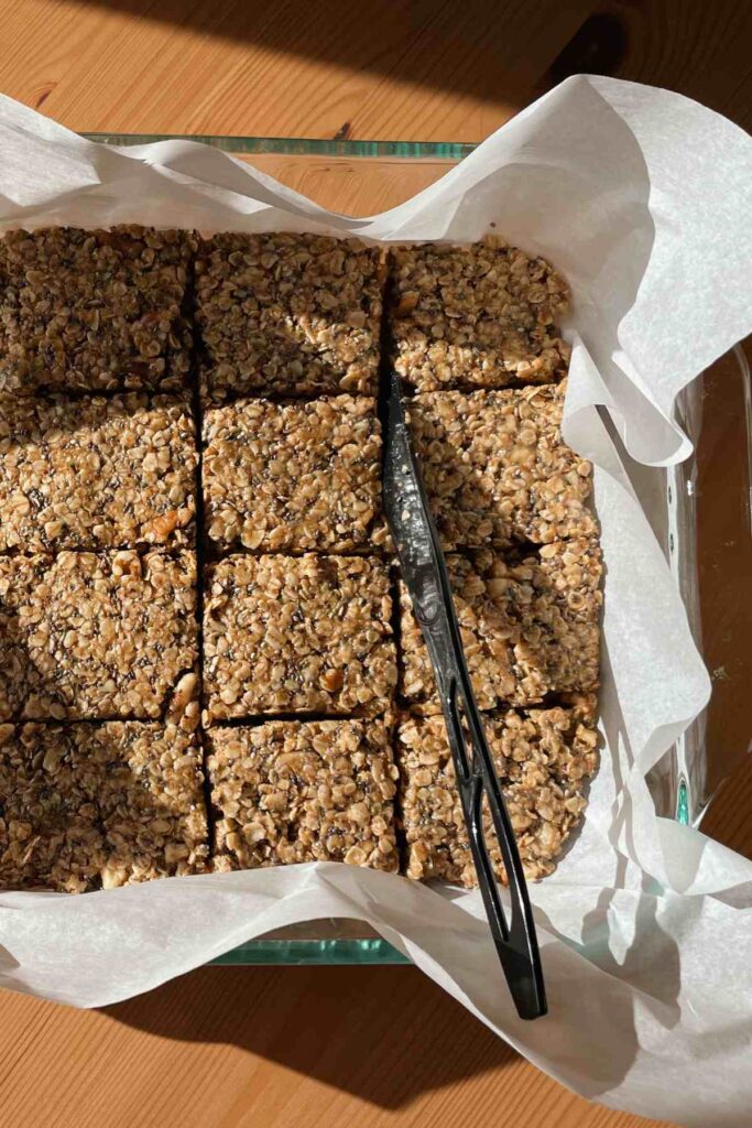 Granola bars in parchment lined baking pan cut into squares with plastic knife