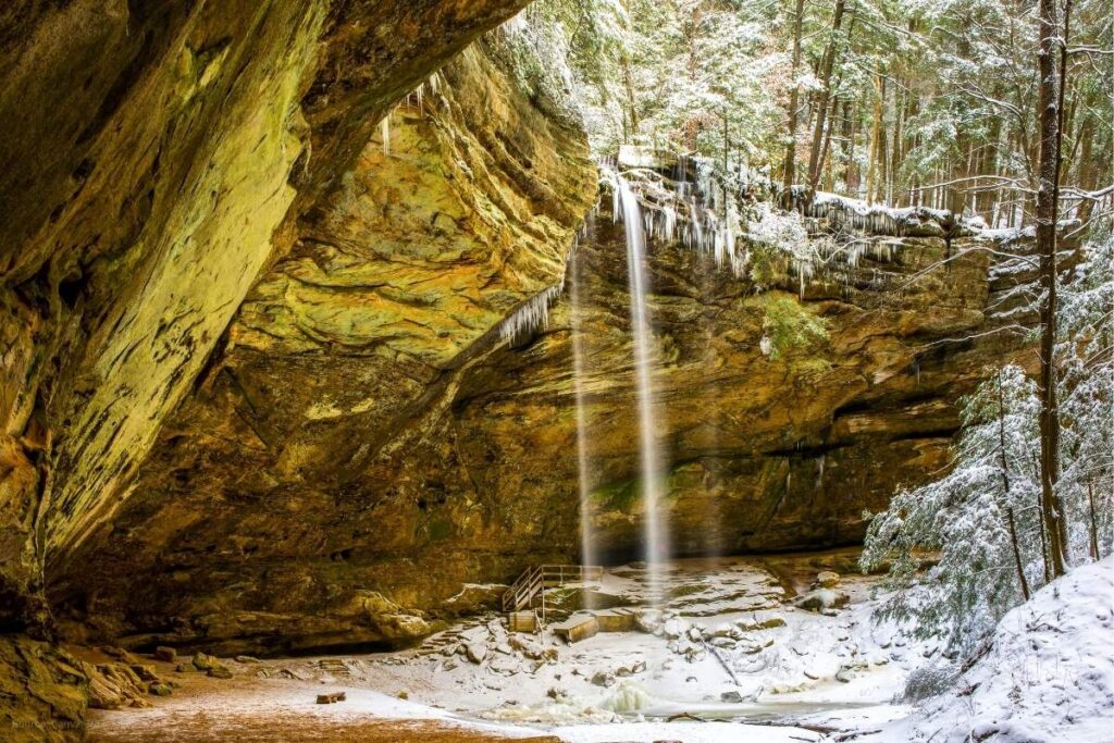 Ash Cave waterfall spilling over rocks into ice covered cave in Hocking Hills Ohio