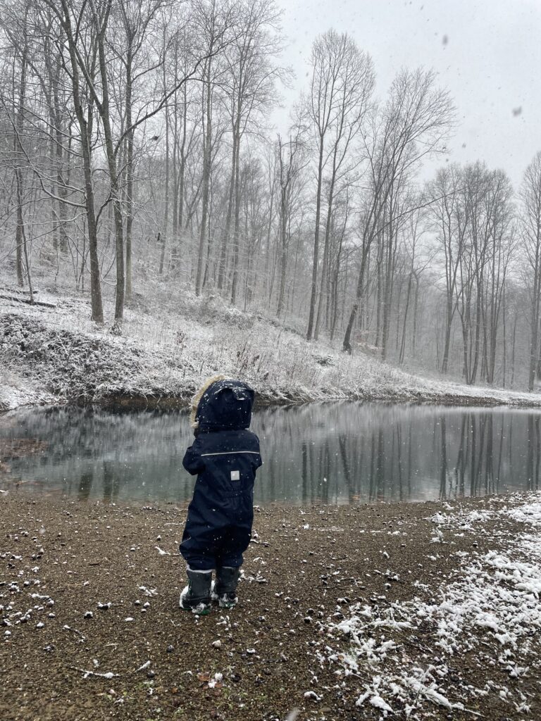 Child in snowsuit facing ice pond