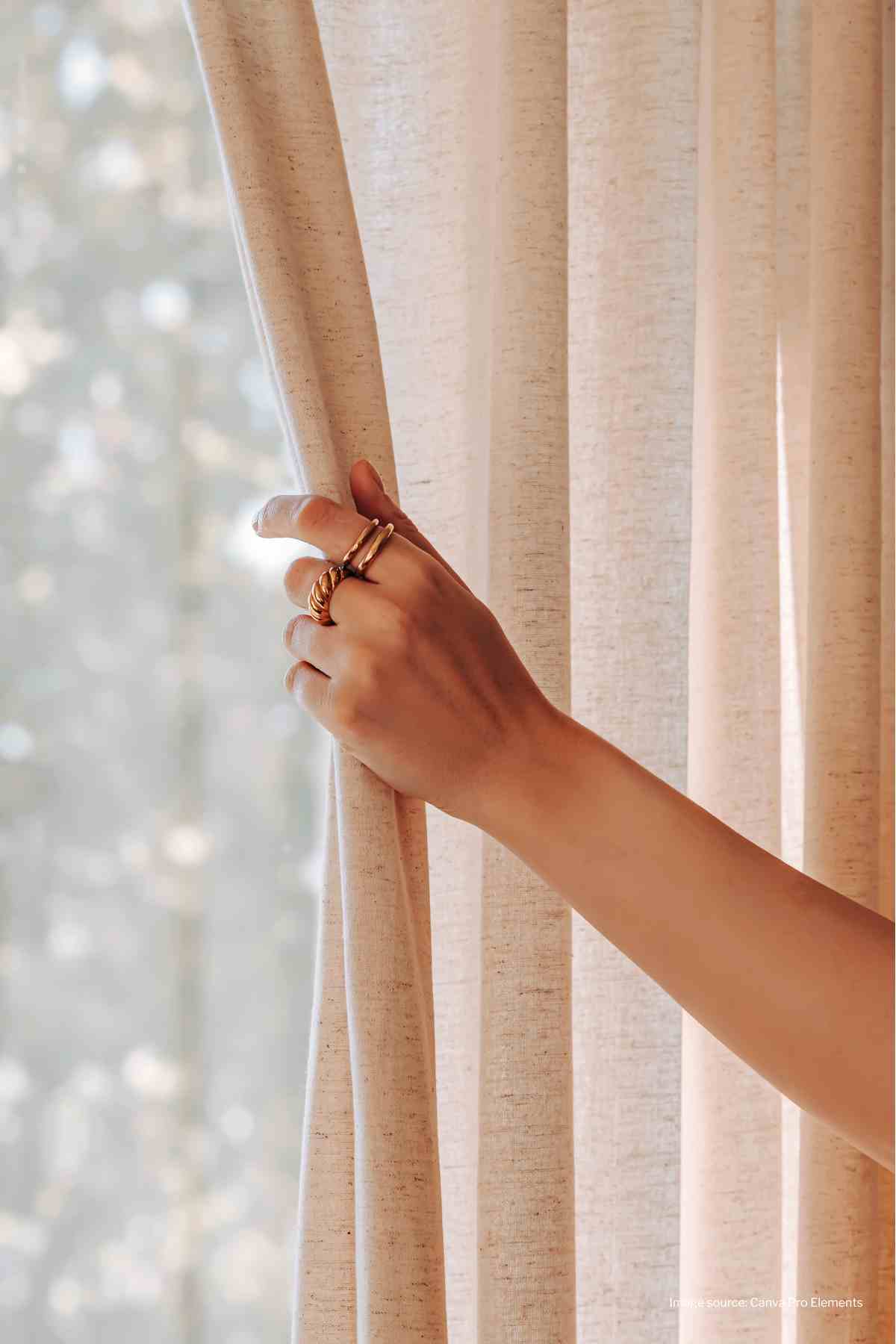 Left hand with rings pulling pale pink curtain open on window
