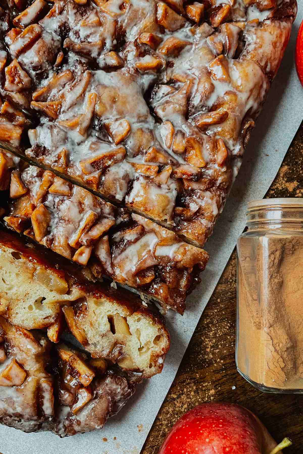 Sourdough apple fritter focaccia sliced on parchment paper with cinnamon and apples around