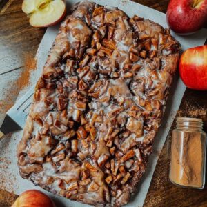 Sourdough apple fritter focaccia on parchment paper surrounded with red apples and ground cinnamon