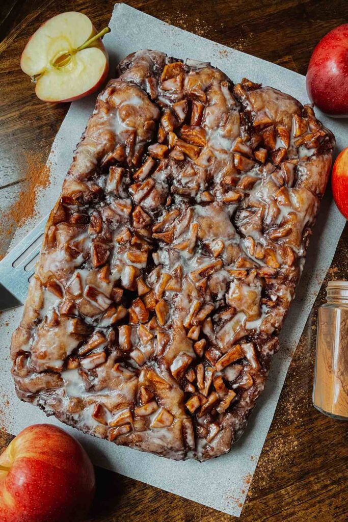 Sourdough apple fritter focaccia on parchment paper surrounded with red apples and ground cinnamon