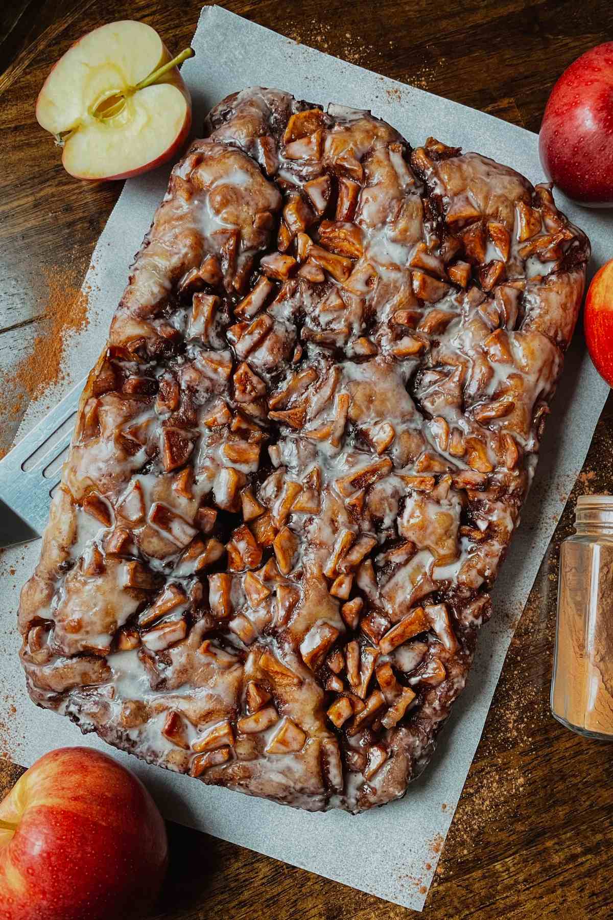 Sourdough apple fritter focaccia on parchment paper surrounded with red apples and ground cinnamon