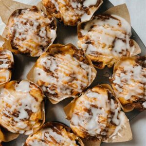 Sourdough coffee cake muffins with vanilla glaze in bakery style brown paper baking cups in metal muffin tin