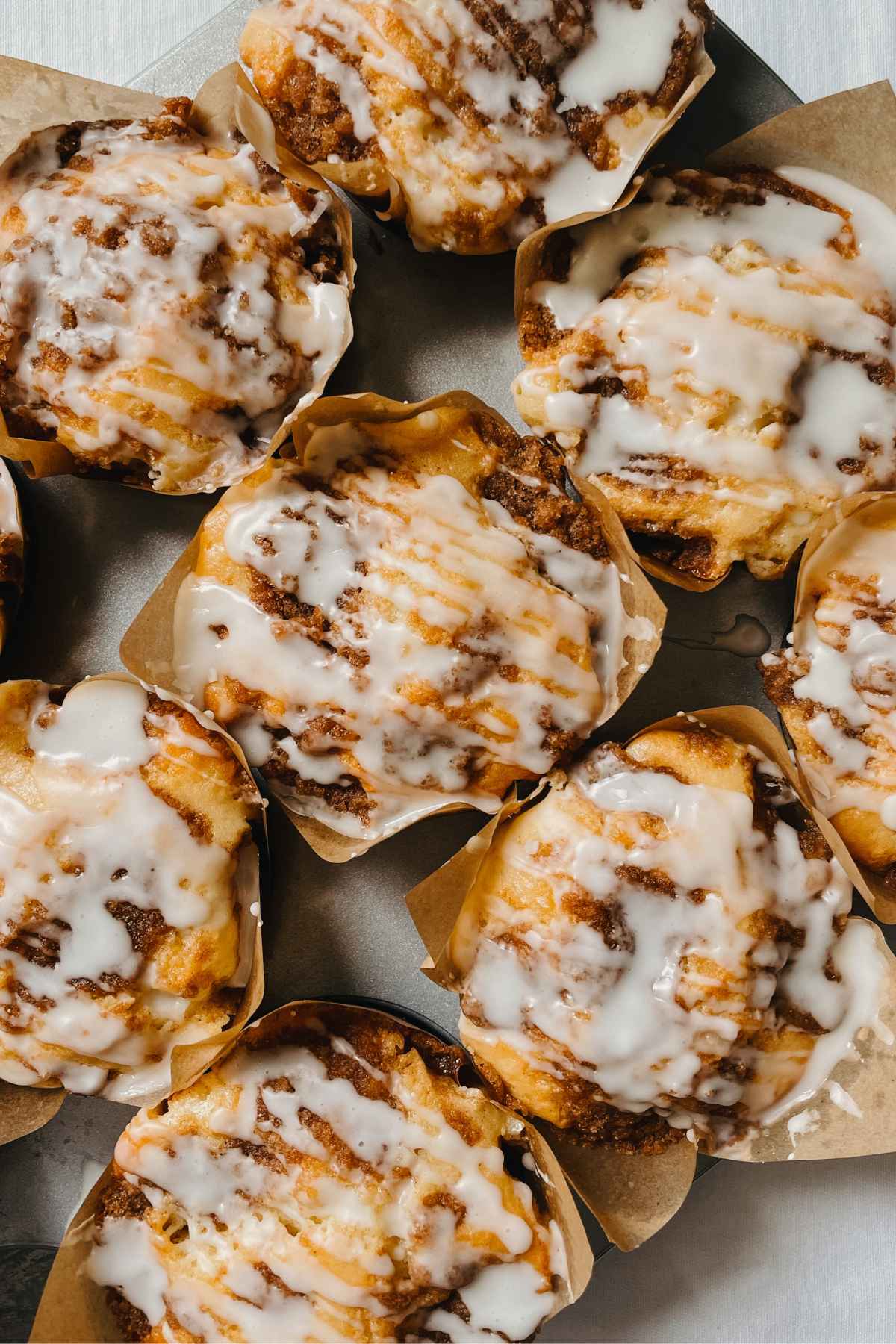 Sourdough coffee cake muffins with vanilla glaze in bakery style brown paper baking cups in metal muffin tin