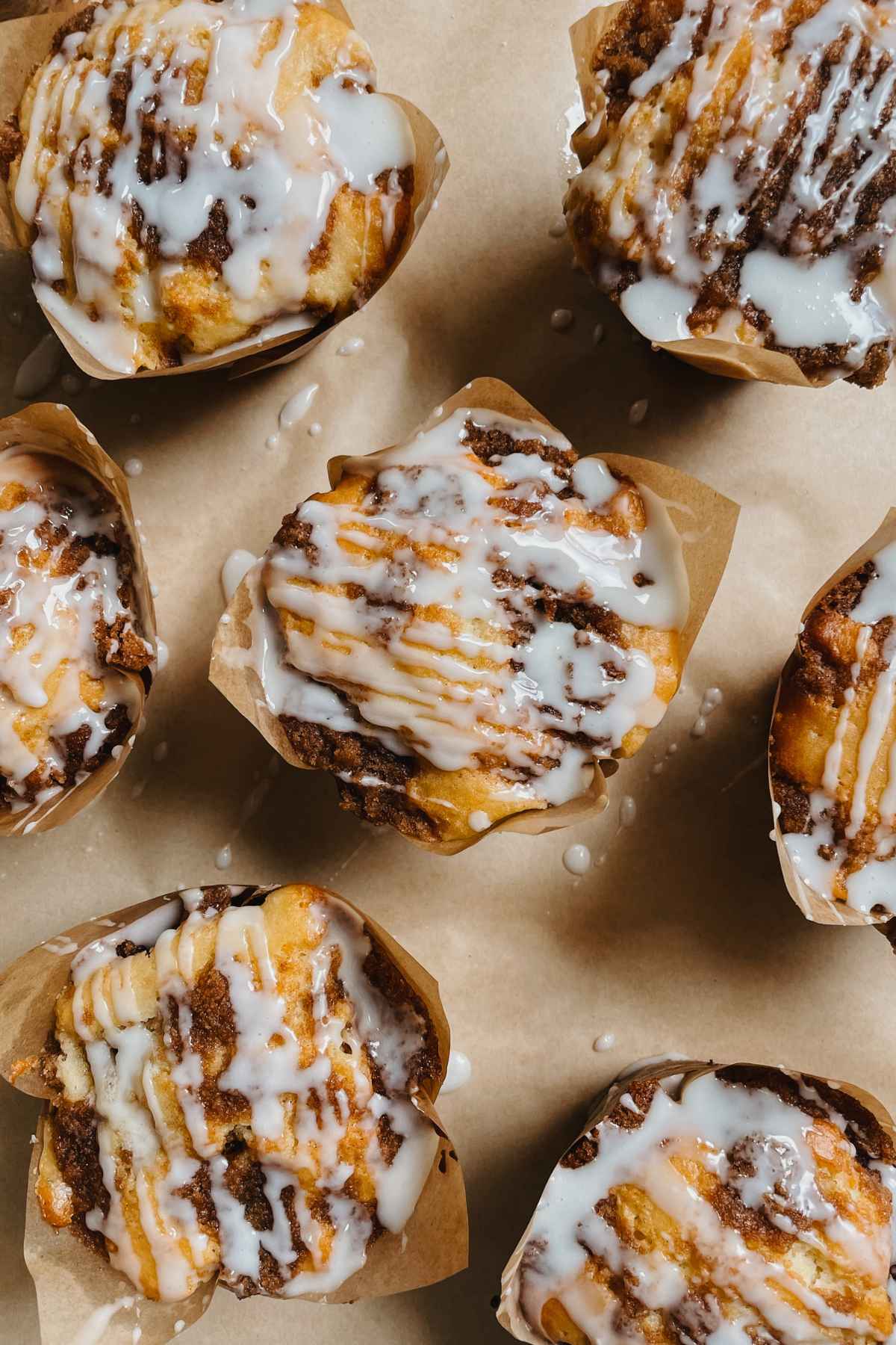 Sourdough coffee cake muffins drizzled with vanilla glaze in bakery style brown paper baking cups sitting on brown parchment paper