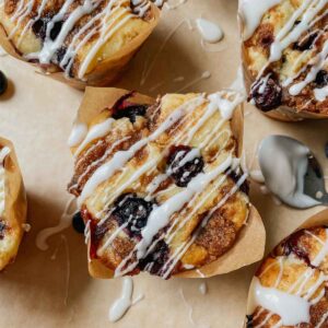 Sourdough blueberry coffee cake muffin with drizzled vanilla glaze sitting on brown parchment paper