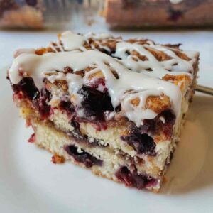 Piece of blueberry sourdough coffee cake with vanilla glaze sitting on a white plate
