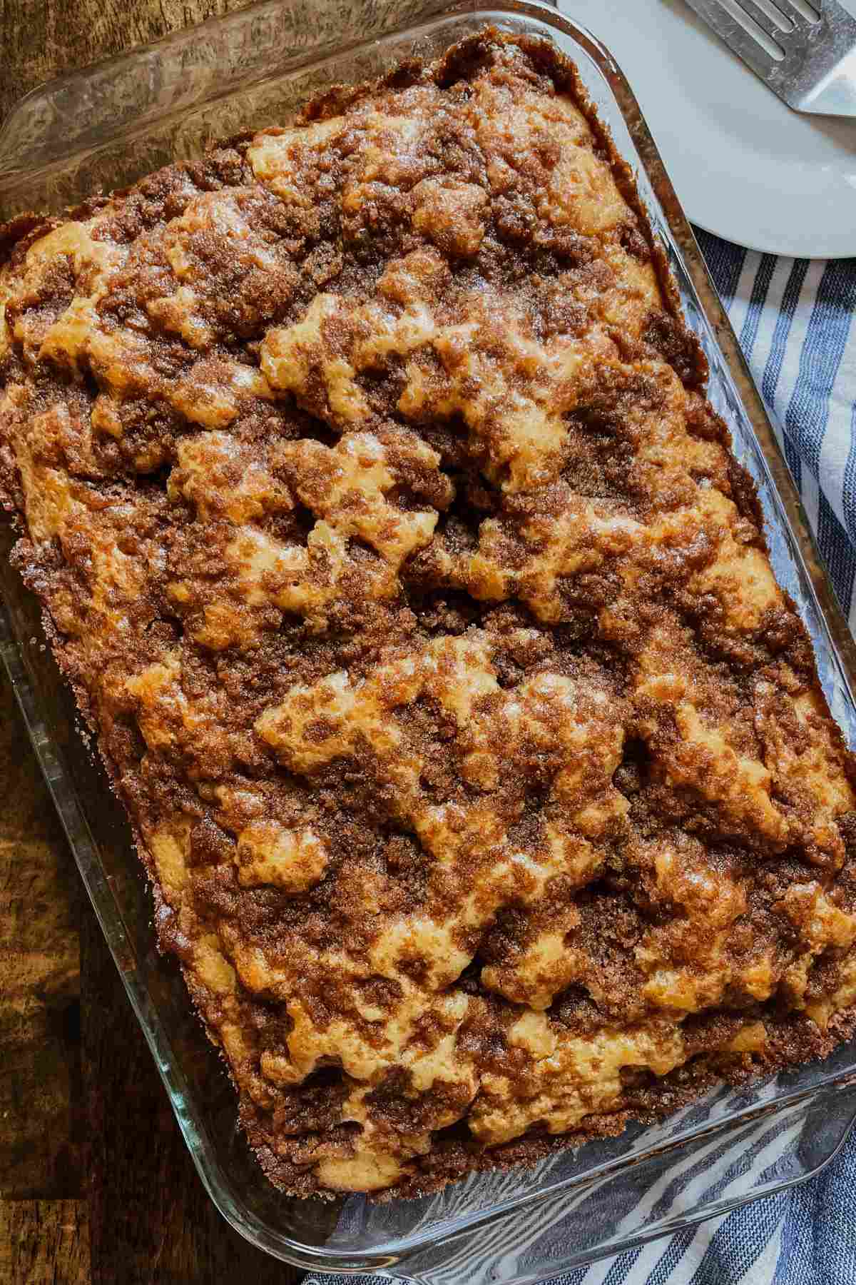 Sourdough discard coffee cake for a crowd topped with cinnamon sugar mixture in glass 9x13 pan with blue and white striped towel on bottom right corner