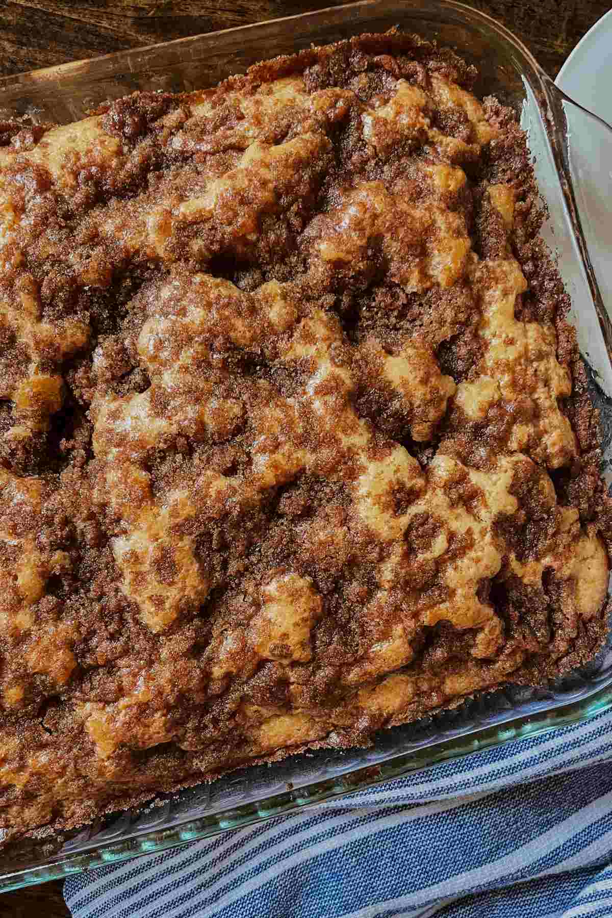 Sourdough discard coffee cake topped with cinnamon sugar mixture with blue and white striped towel on bottom right corner