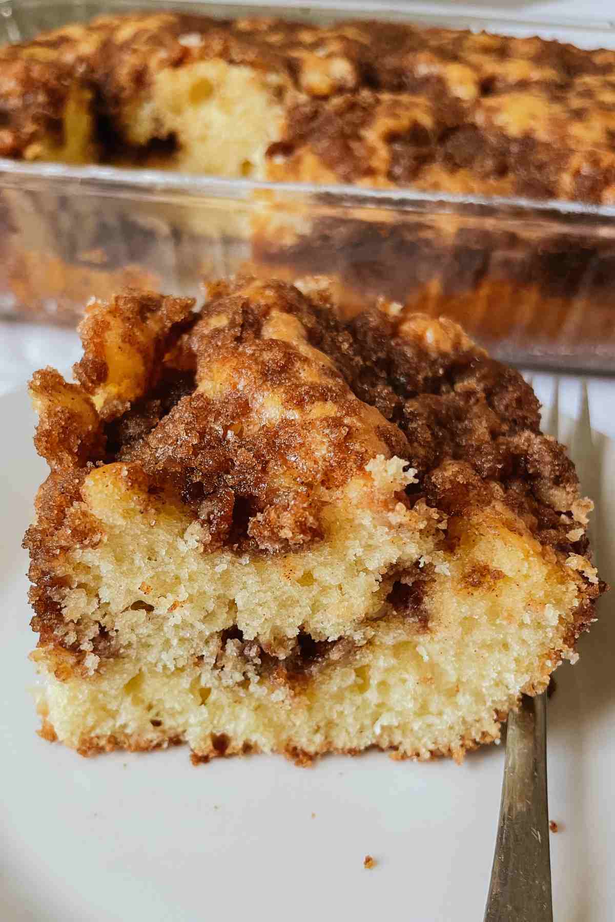 Sourdough discard coffee cake slice with fluffy sourdough coffee cake filled with cinnamon sugar crumble filling and topped with cinnamon sugar mixture on a white plate with a silver fork