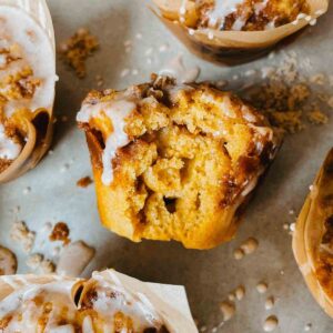 Sourdough pumpkin coffee cake muffin on it's side on parchment paper with other muffins and cinnamon vanilla glaze drizzled around