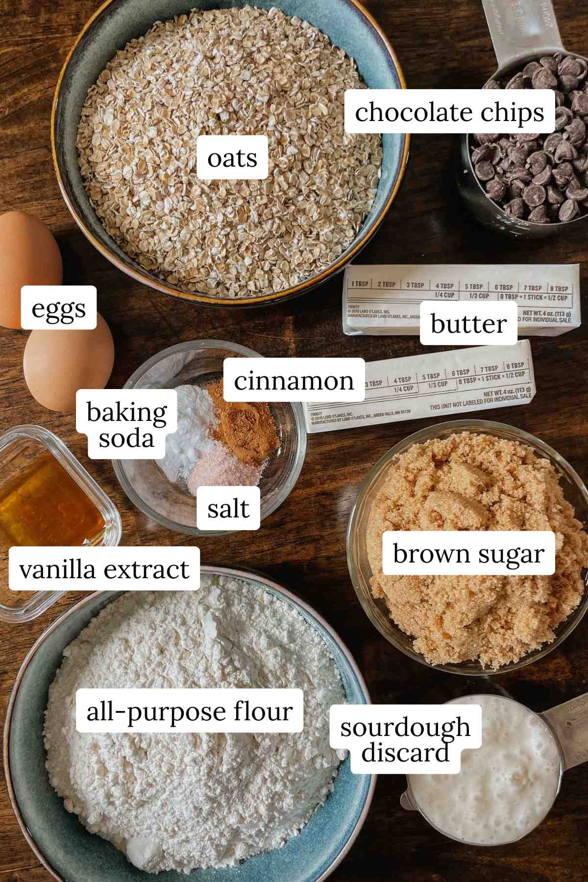Ingredients for sourdough oatmeal chocolate chip cookie bars labeled on a wooden table