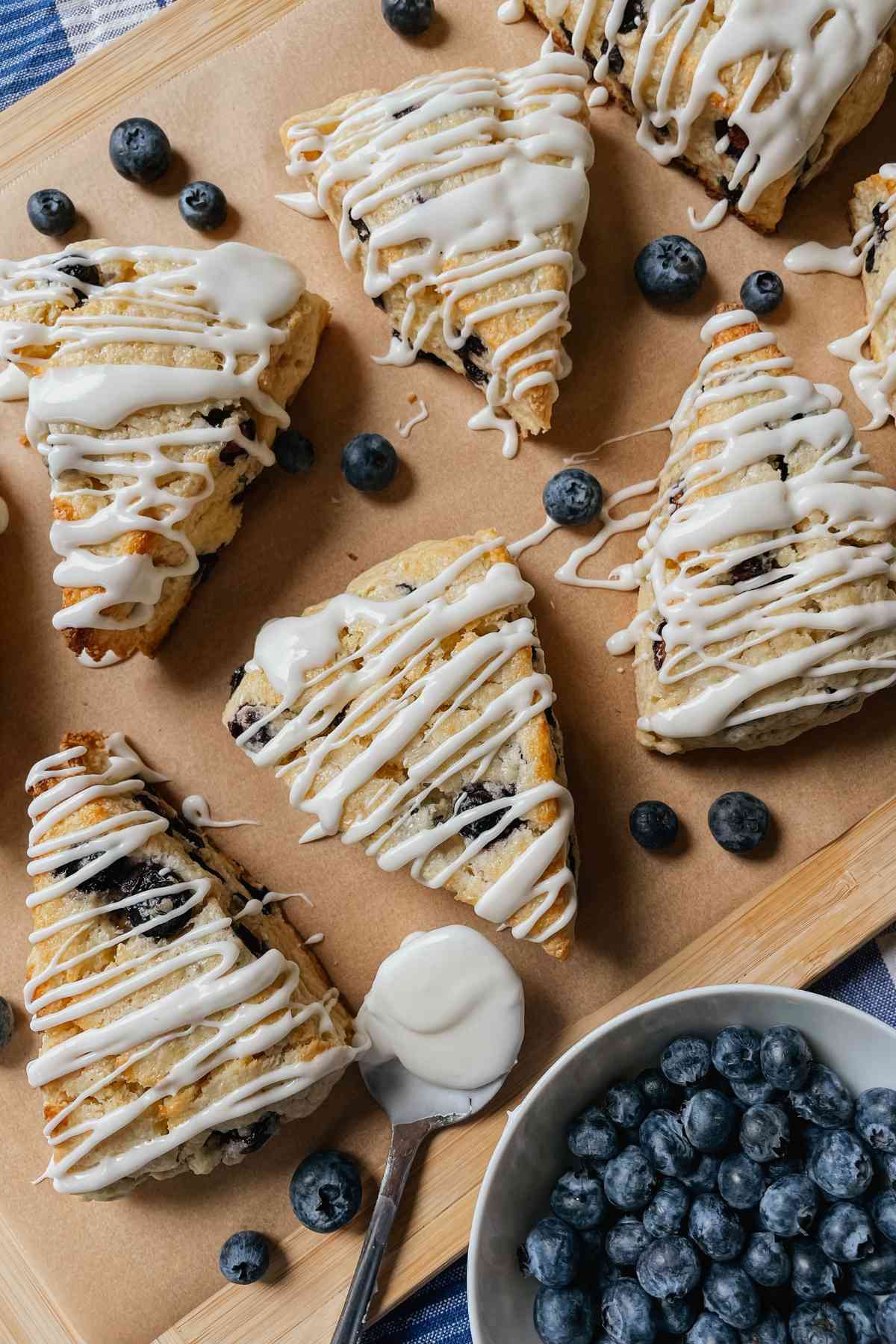 Sourdough blueberry scones drizzled with sweet glaze on parchment paper with blueberries sprinkled around