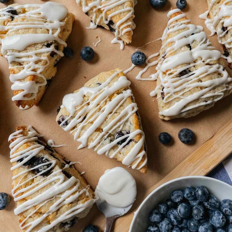 Sourdough blueberry scones drizzled with sweet glaze on parchment paper with blueberries sprinkled around