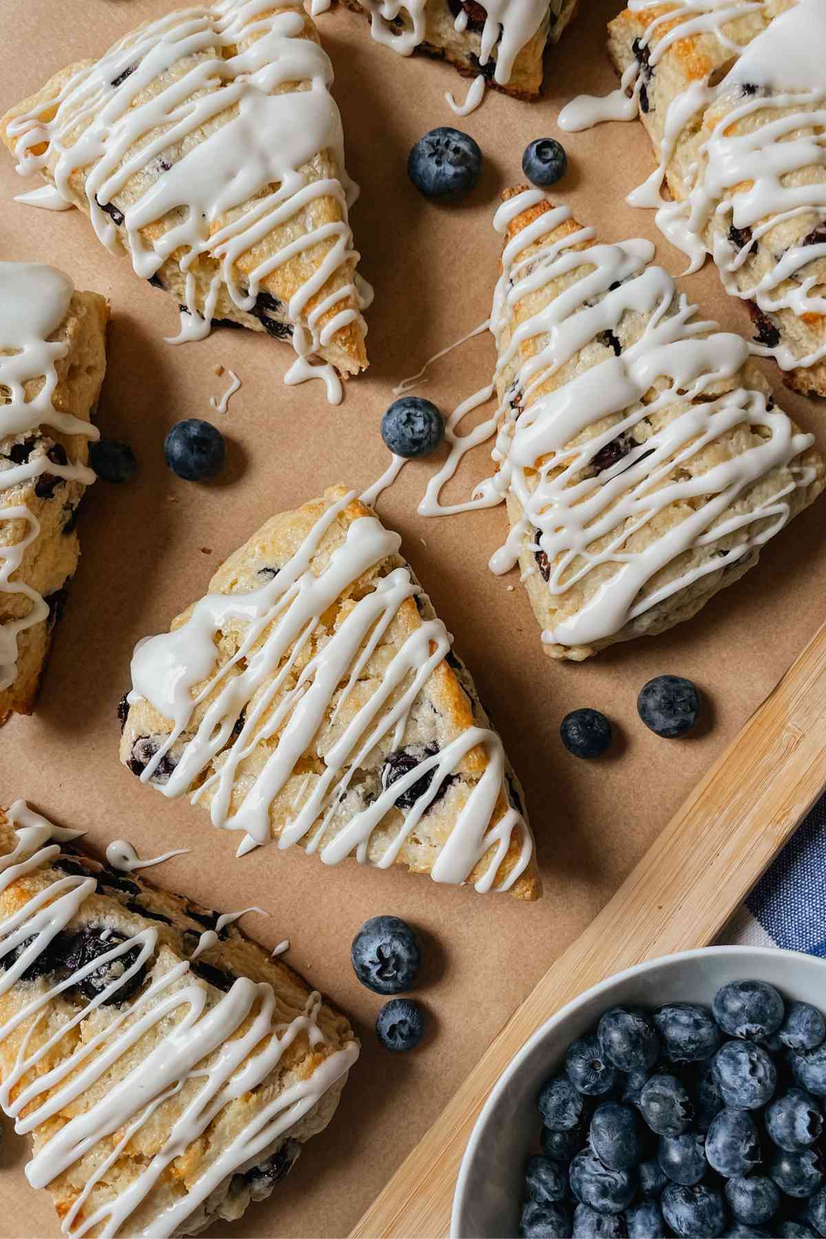 Blueberry sourdough scones drizzled with sweet glaze on parchment paper with blueberries sprinkled around