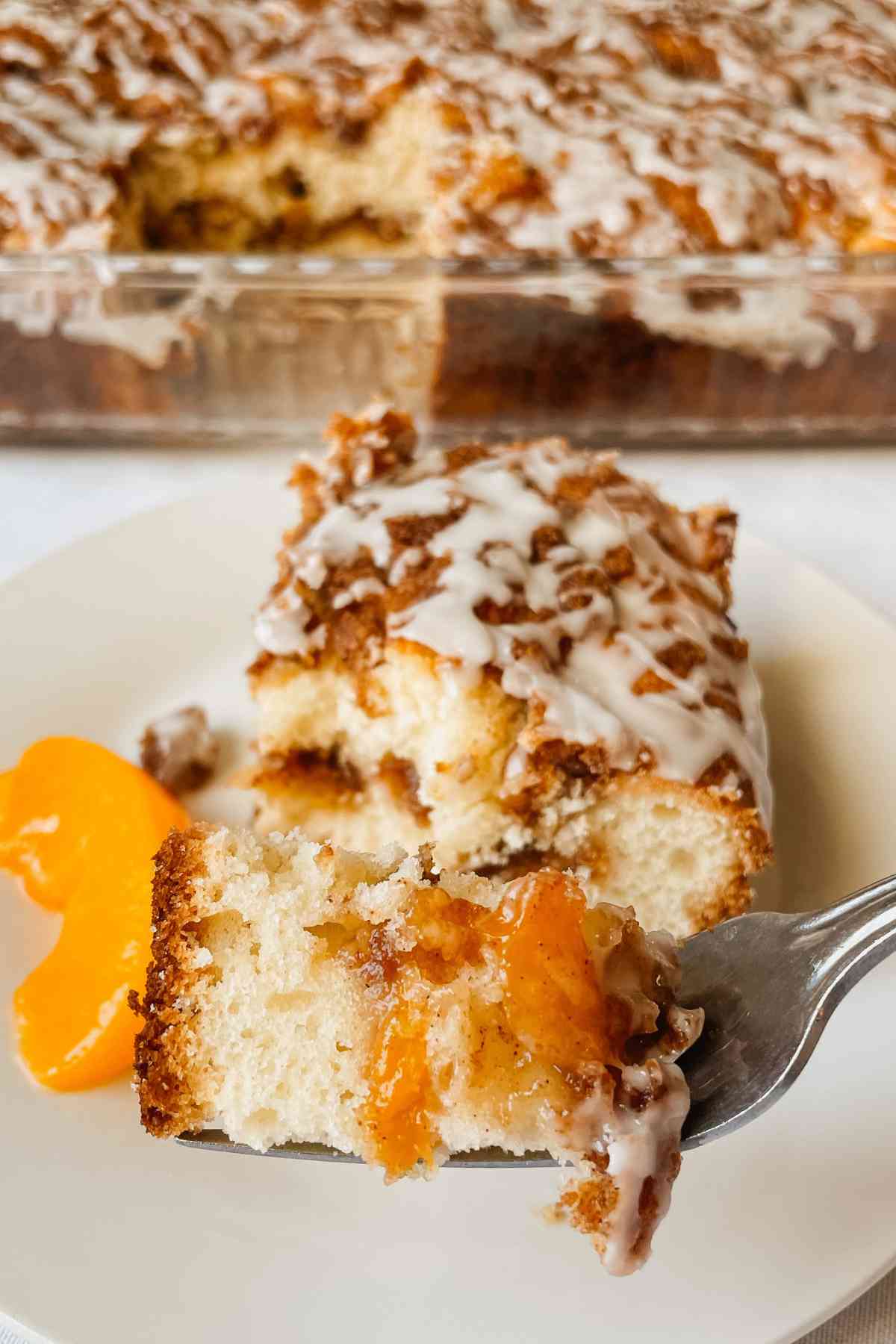 Bite of sourdough peach coffee cake drizzled with vanilla glaze on a fork