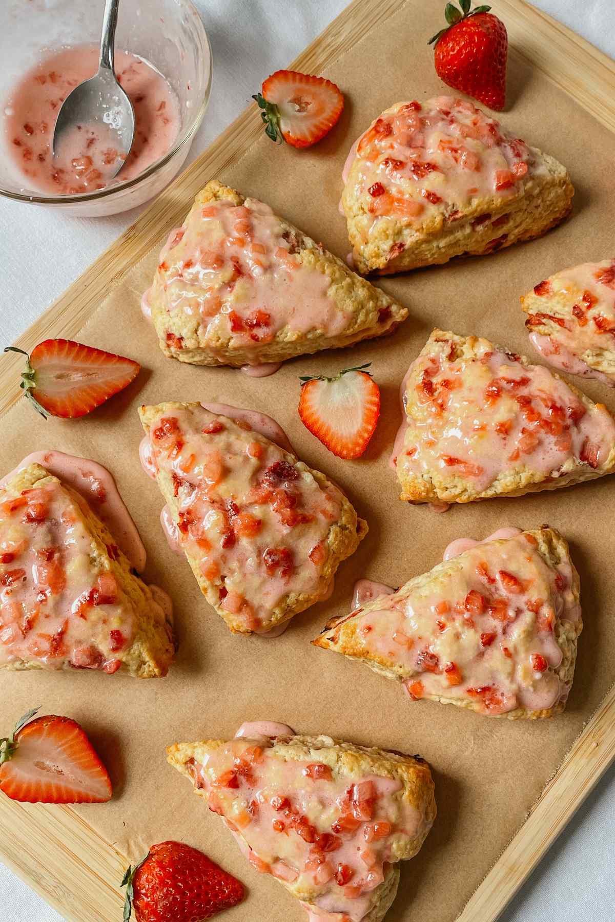 Sourdough strawberry scones drizzled with strawberry glaze on parchment paper with strawberries sprinkled around