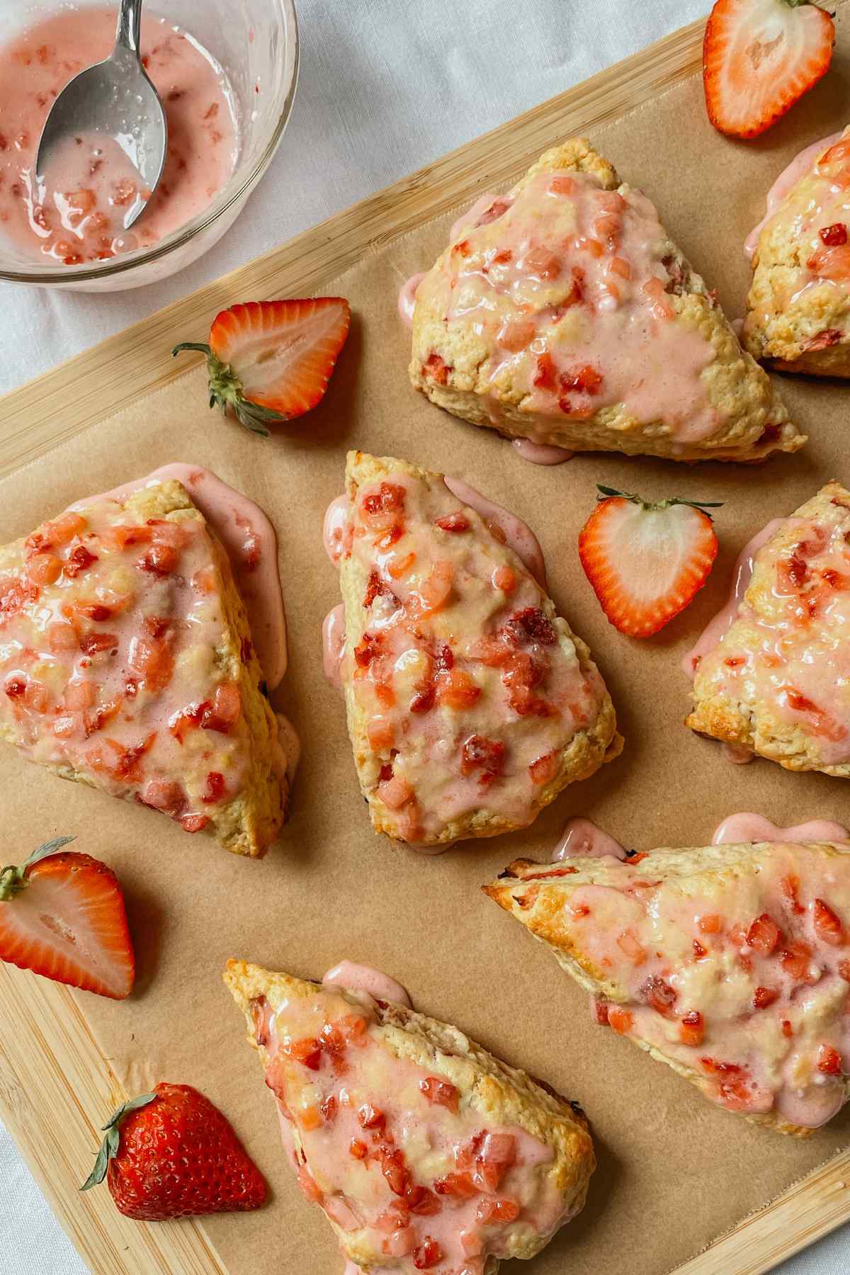 Strawberry sourdough scones drizzled with strawberry glaze on parchment paper with strawberries sprinkled around