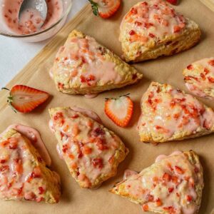 Sourdough strawberry scones drizzled with strawberry glaze on parchment paper with strawberries sprinkled around