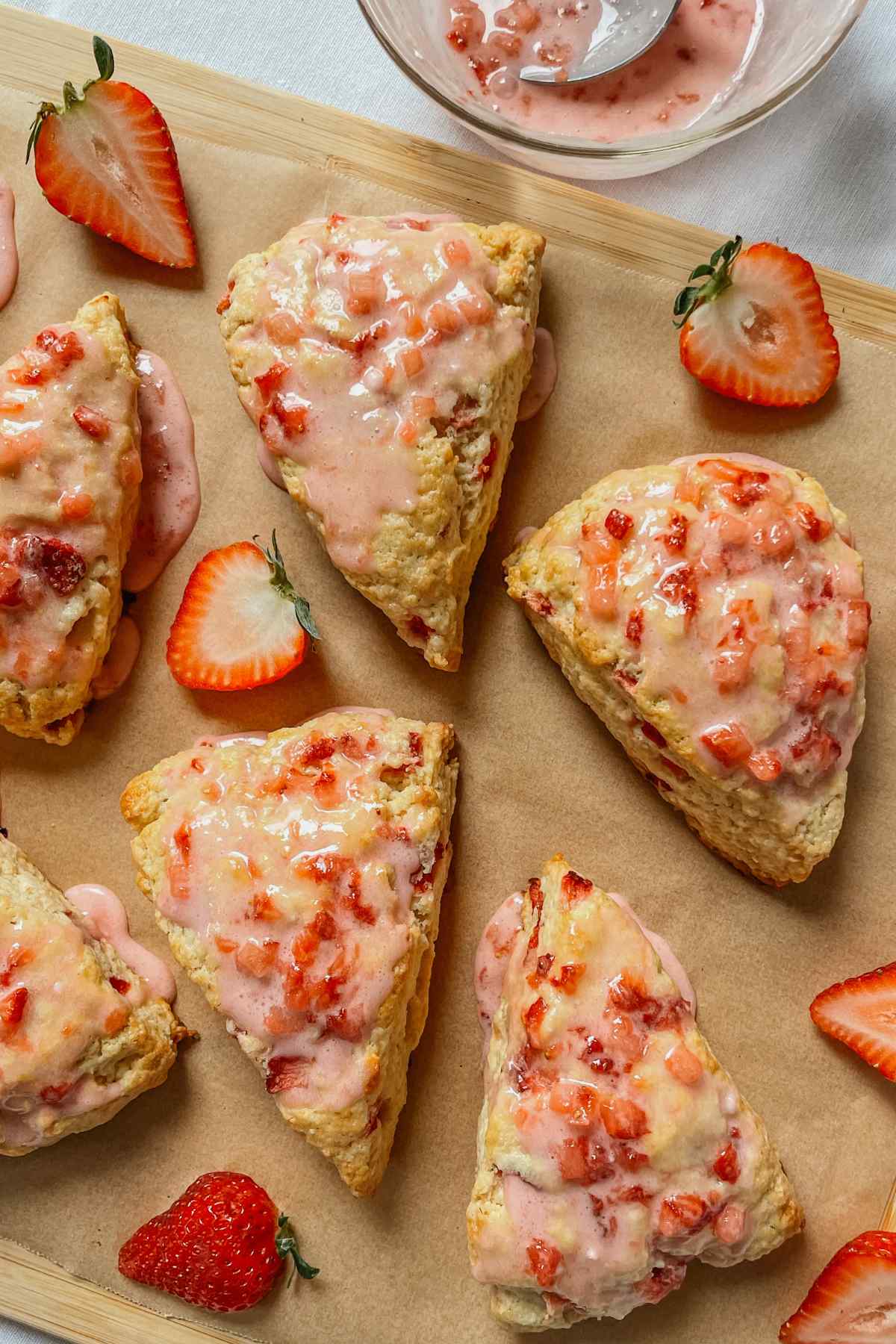 Strawberry sourdough scones drizzled with strawberry glaze on parchment paper with strawberries sprinkled around