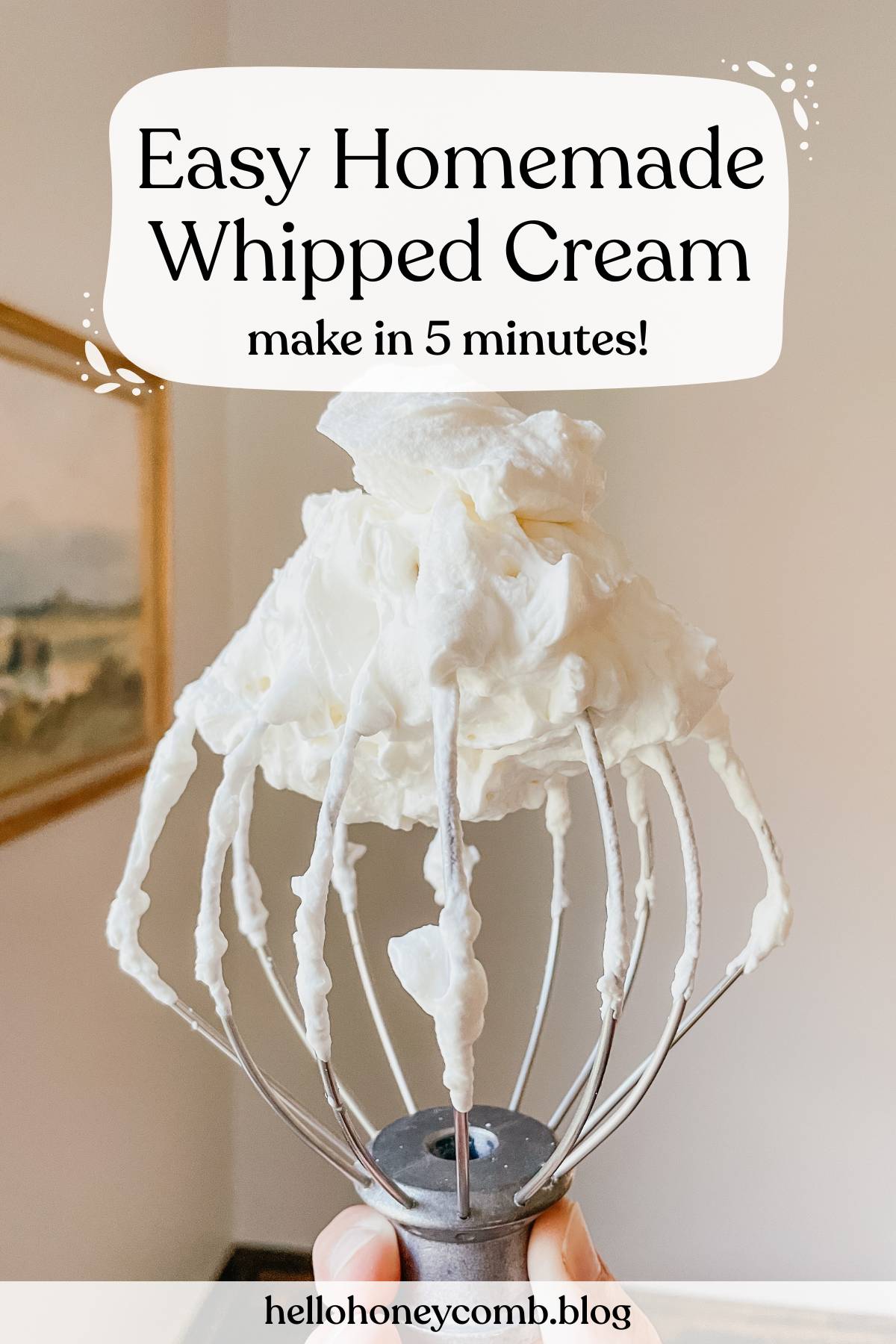 Hand holding a wire whisk with homemade whipped cream in front of a wall with text overlaid that reads Easy Homemade Whipped Cream make in 5 minutes!