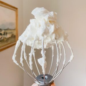 Wire whisk with homemade whipped cream in front of a wall