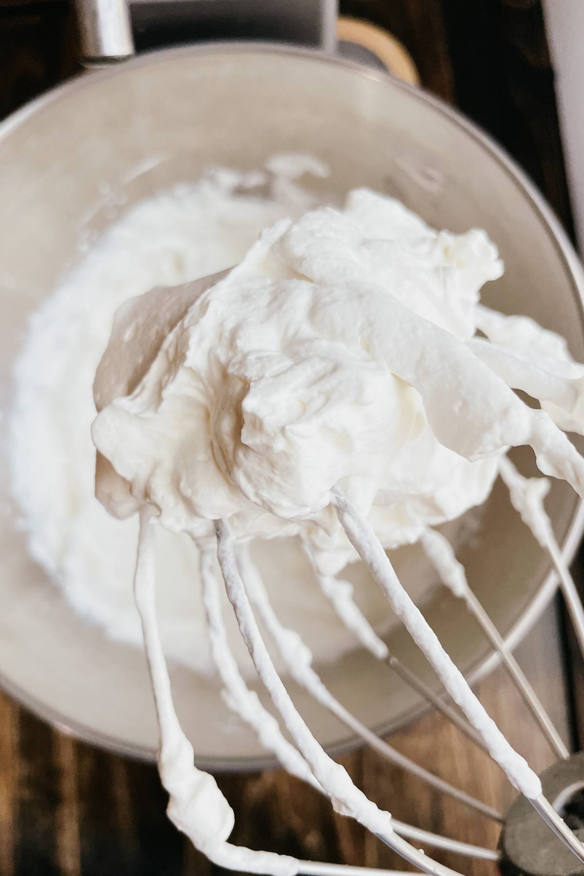 Close up of homemade whipped cream on wire whisk attachment with kitchen mixer in background