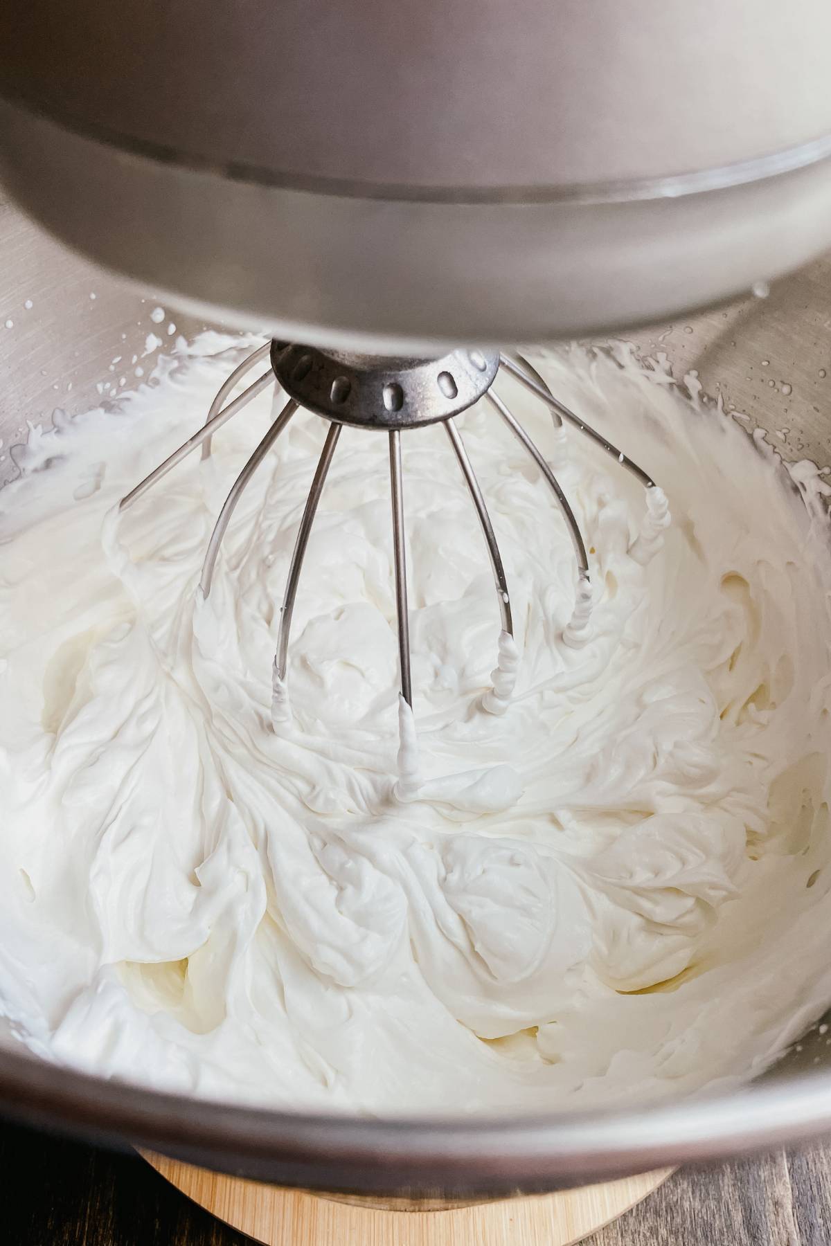 Kitchen stand mixer with homemade whipped cream in metal mixing bowl being whisked with wire whisk attachment