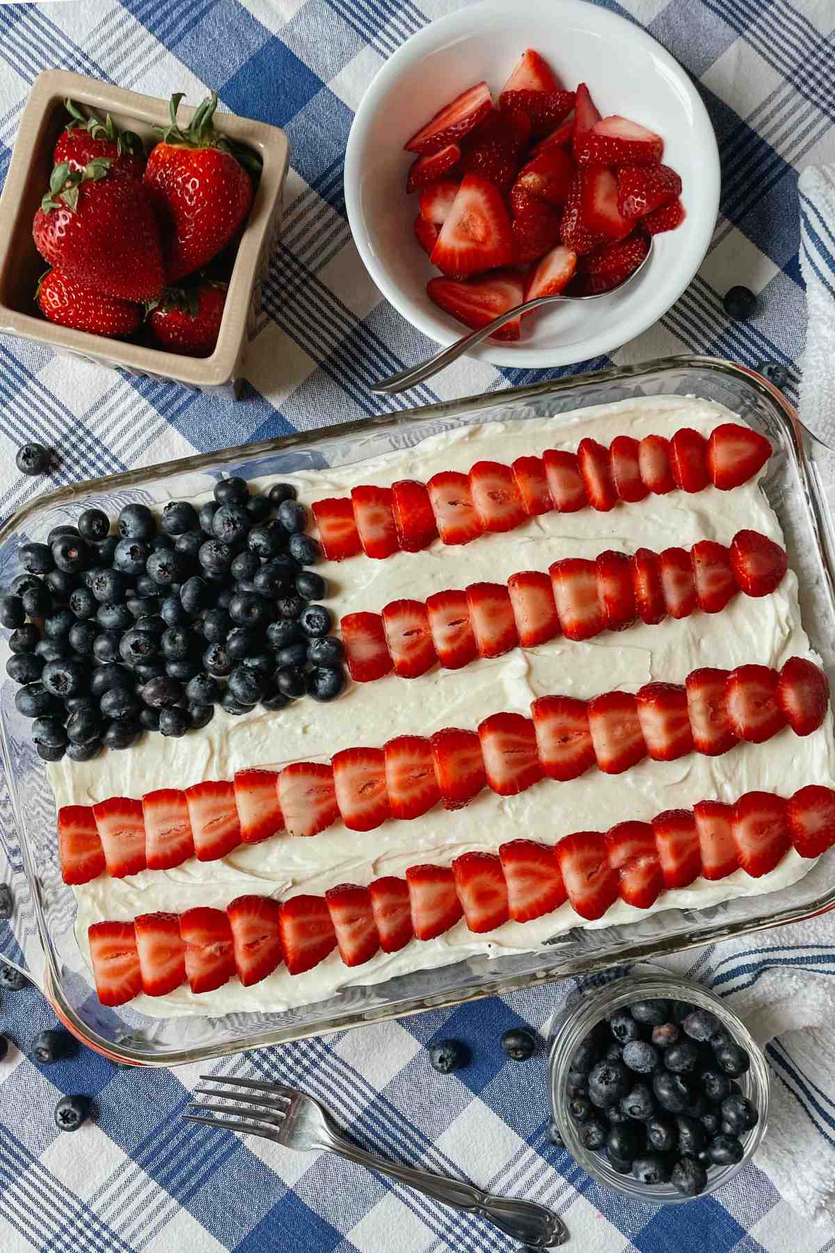 Sourdough American flag cake on blue checkered tablecloth with blueberries and strawberries in bowls