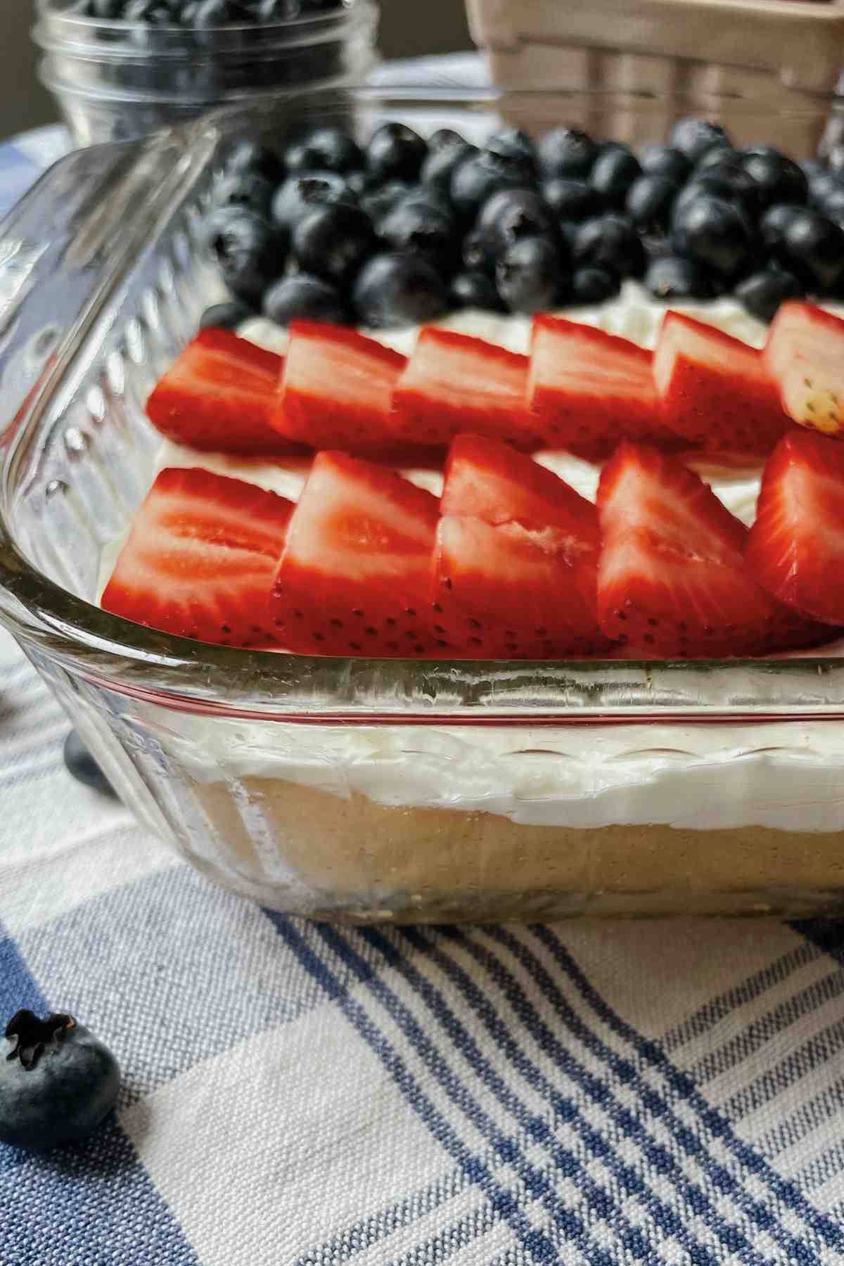 Side of pan of sourdough shortcake with layers of vanilla shortcake, cream cheese icing, and topping with berrie