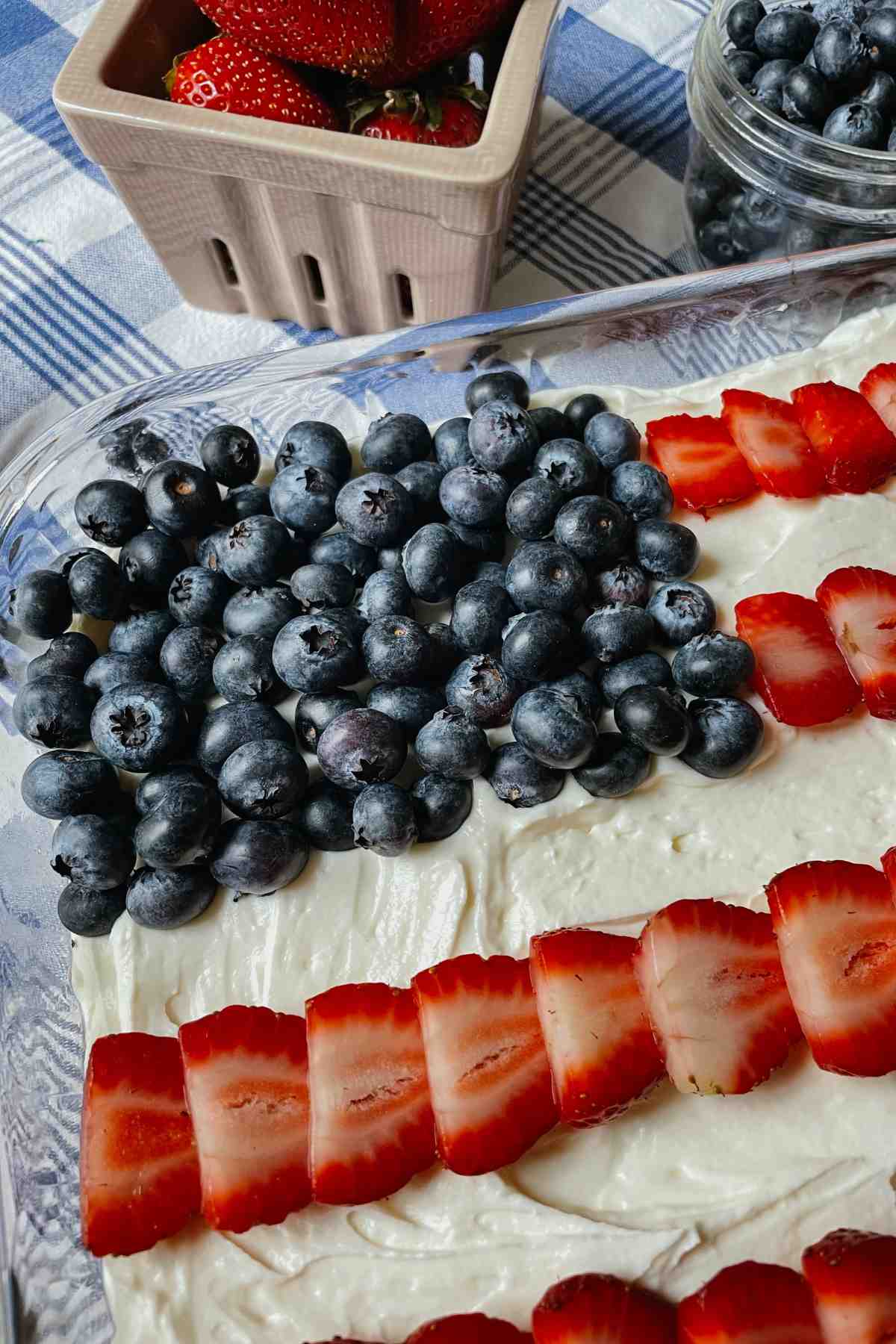 Close up of blueberries on sourdough American flag cake on blue checkered tablecloth with berries in background