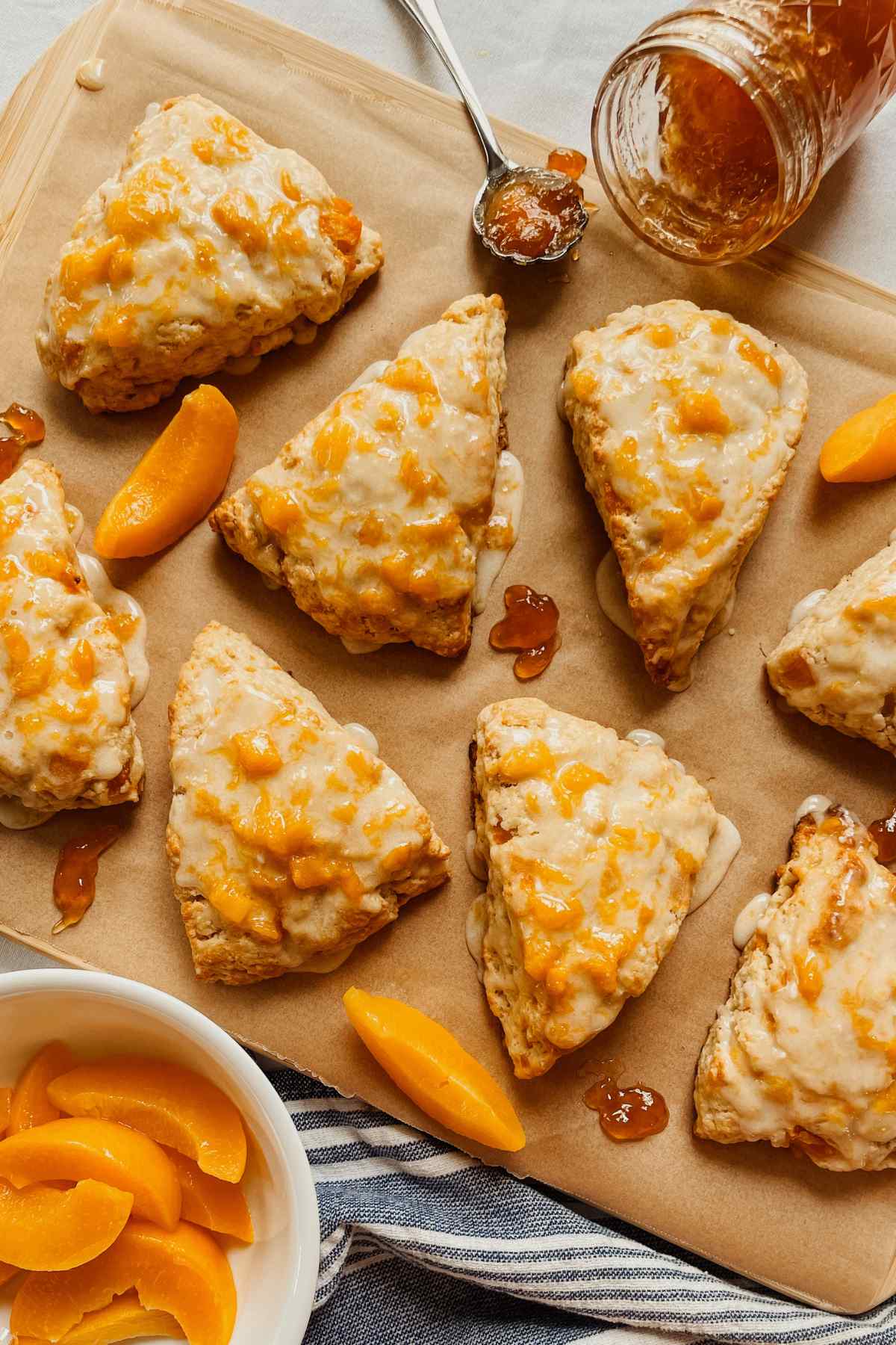 Sourdough peach scones drizzled with peach glaze on parchment paper with peach slices and peach jam sprinkled around