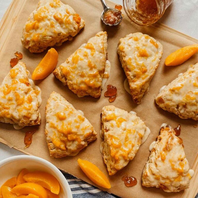 Sourdough peach scones drizzled with peach glaze on parchment paper with peach slices and peach jam sprinkled around