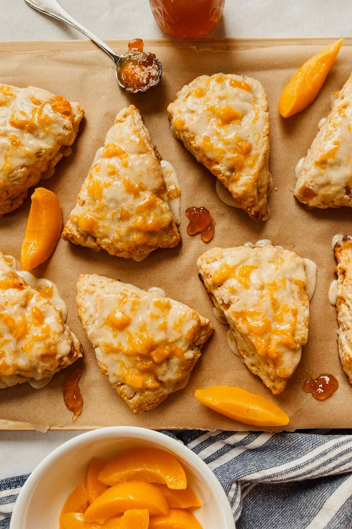 Sourdough peach scones drizzled with peach glaze on parchment paper with peach slices and peach jam sprinkled around