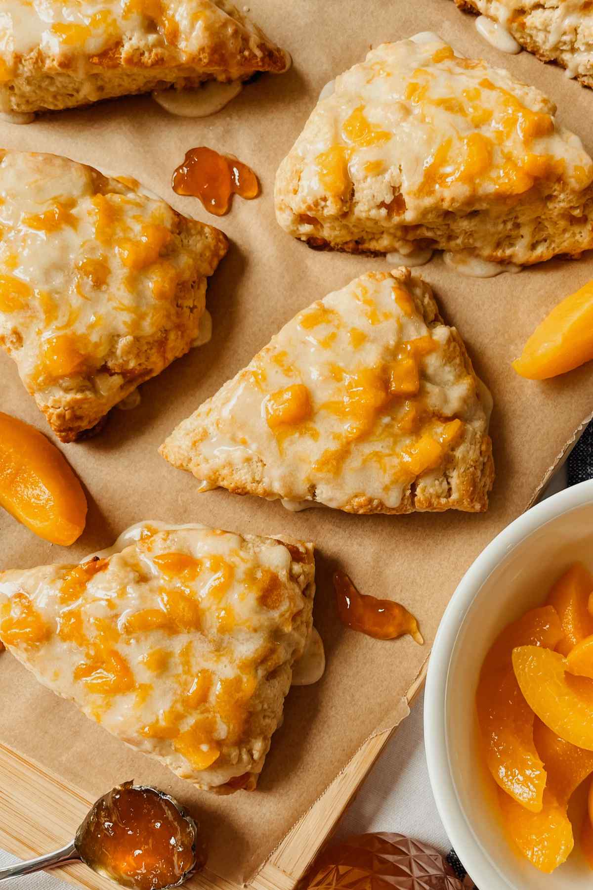 Peach sourdough scones drizzled with peach glaze on parchment paper with peach slices and peach jam sprinkled around