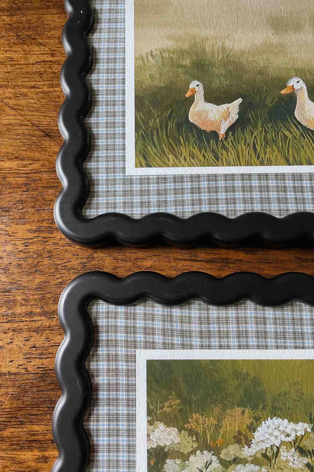 Corners of black wavy picture frames with plaid fabric picture frame mats and art print of ducks and wildflowers