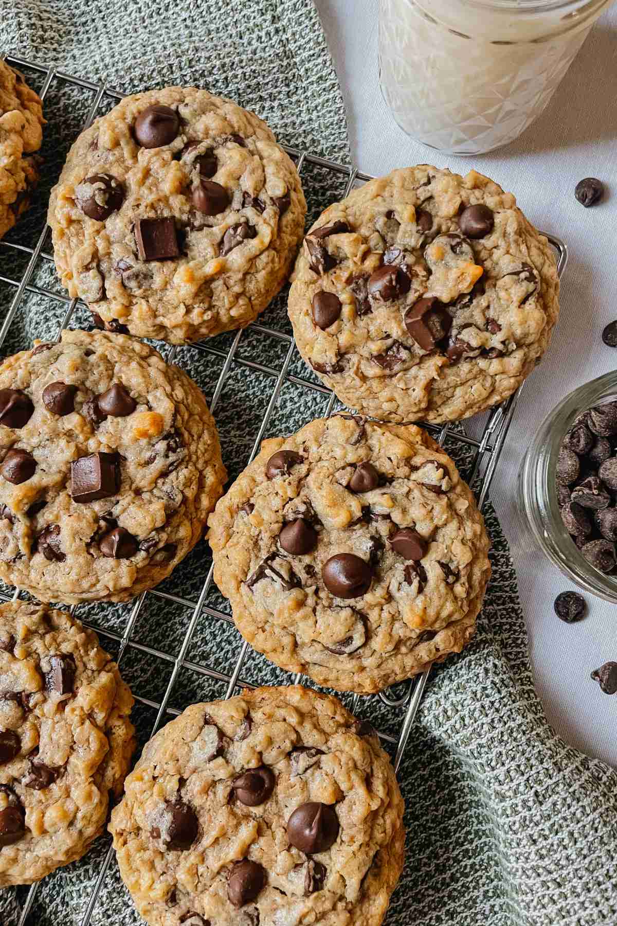 Sourdough peanut butter oatmeal chocolate chip cookies on wire rack with kitchen towel, chocolate chips, and glass of milk around