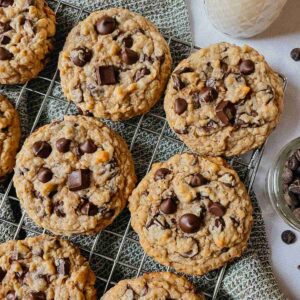 Sourdough peanut butter oatmeal chocolate chip cookies on wire rack with kitchen towel, chocolate chips, and glass of milk around