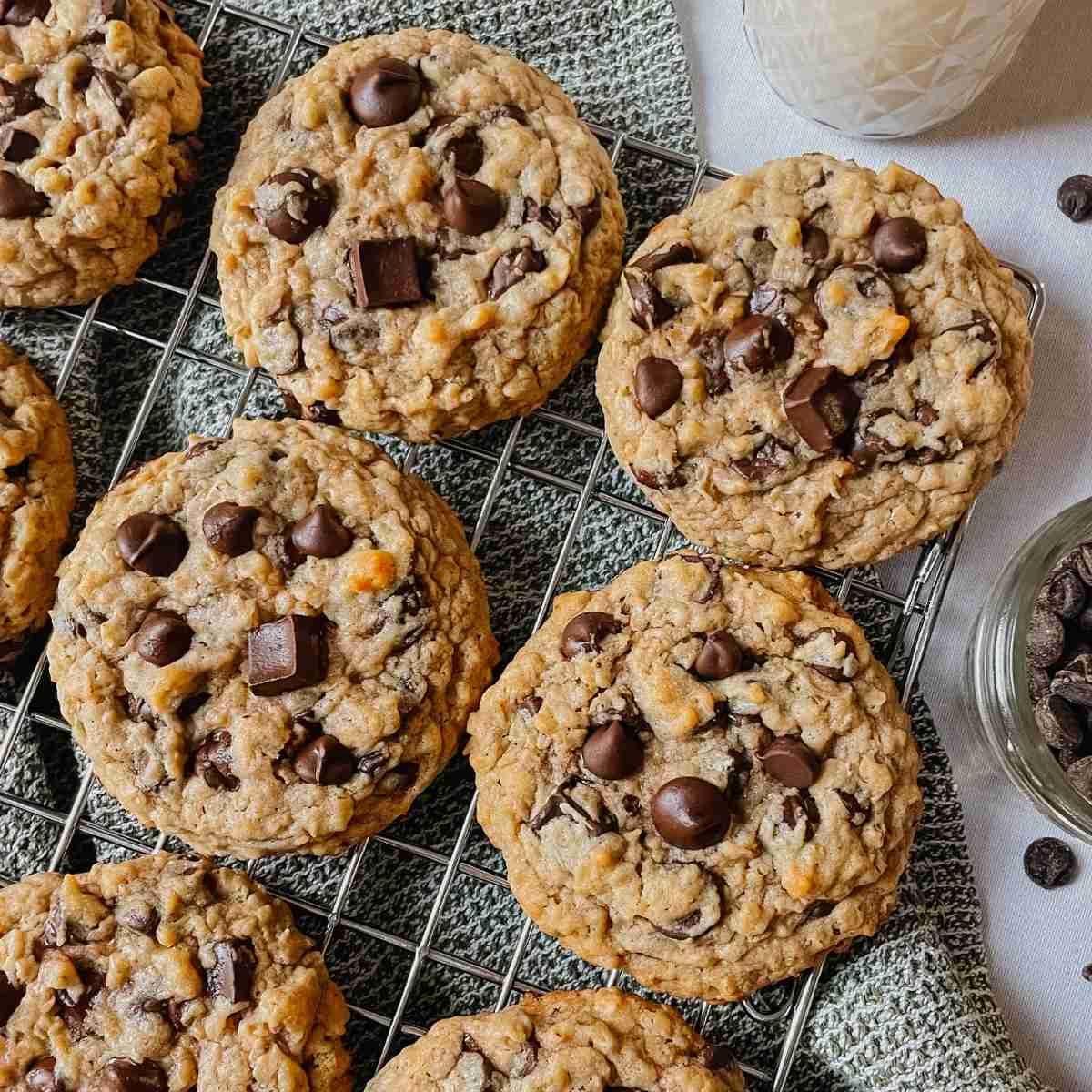 Sourdough peanut butter oatmeal chocolate chip cookies on wire rack with kitchen towel, chocolate chips, and glass of milk around