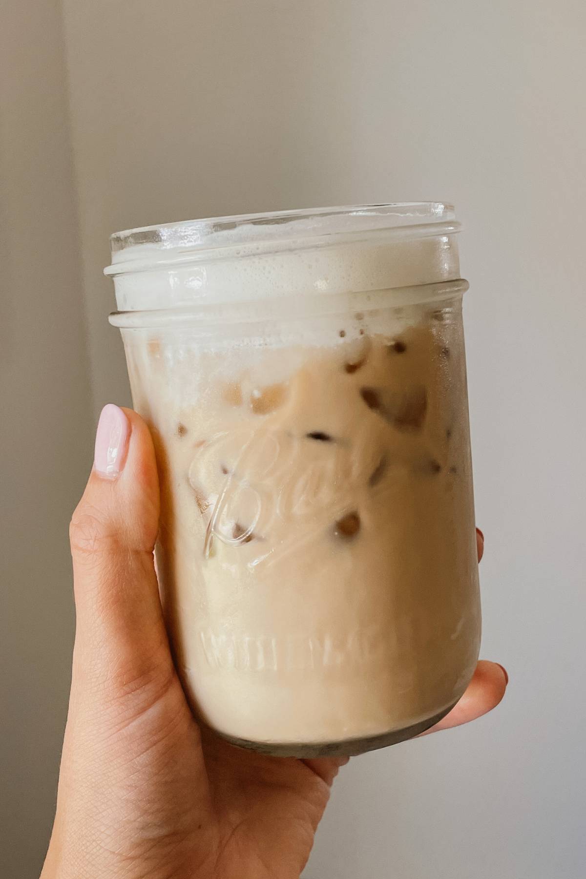 Hand holding glass mason jar of iced coffee with brown sugar coffee syrup
