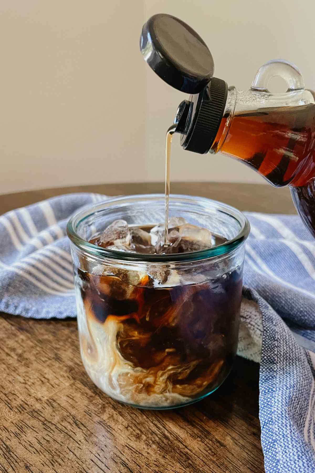Glass bottle pouring brown sugar coffee syrup into a glass of iced coffee