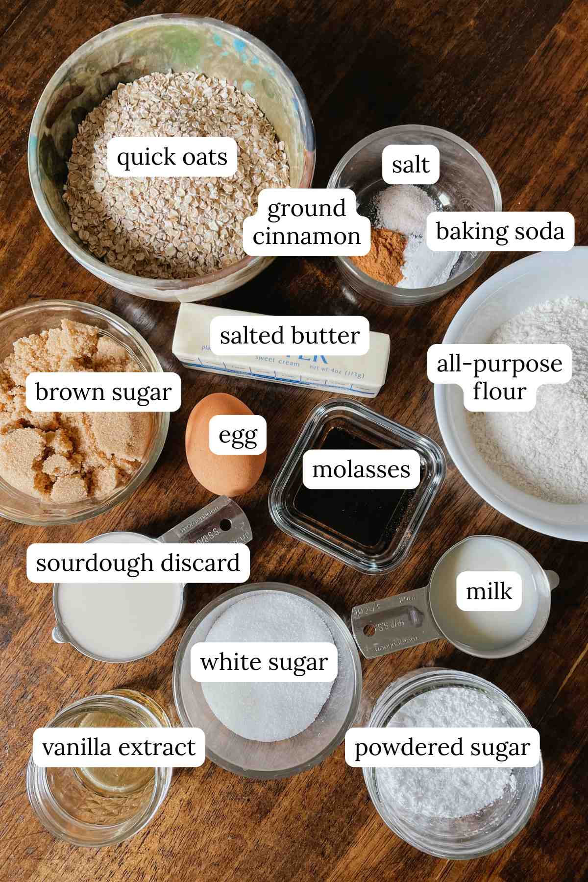 Ingredients for sourdough iced oatmeal cookie bars in bowls labeled on wooden table