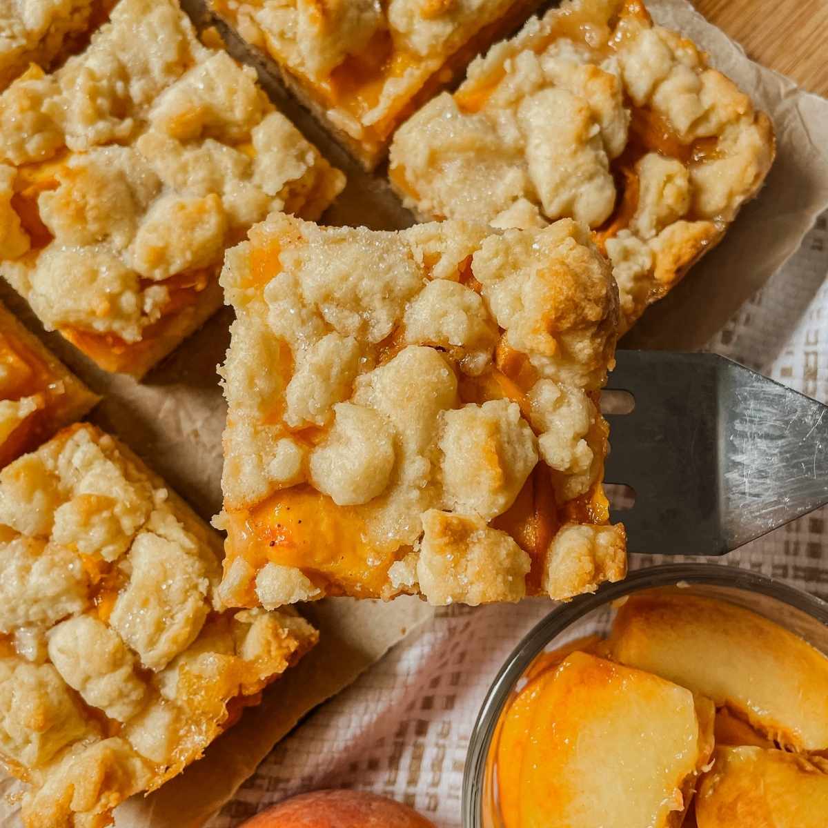 Sourdough peach crumb bar square held up on a square server with peaches in background