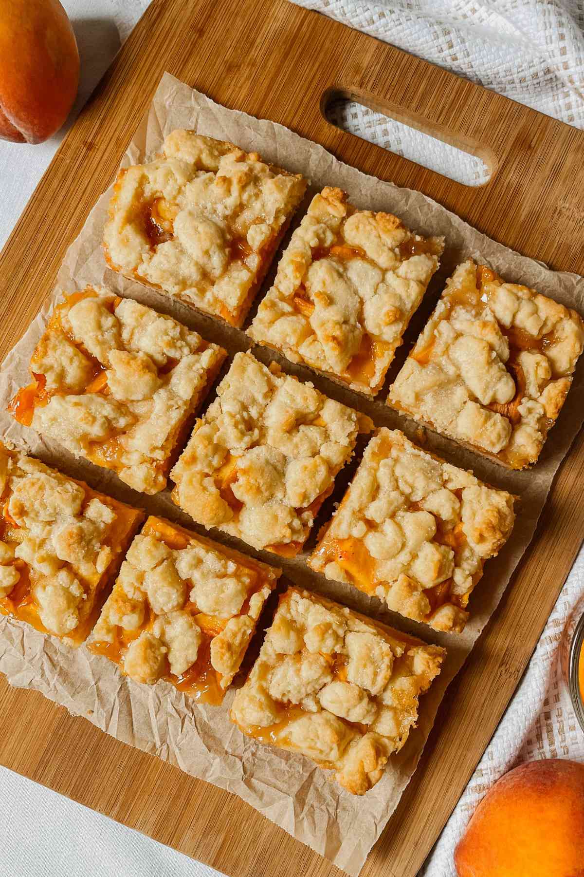 Sourdough peach crumb bars cut into squares on parchment paper on wooden cutting board