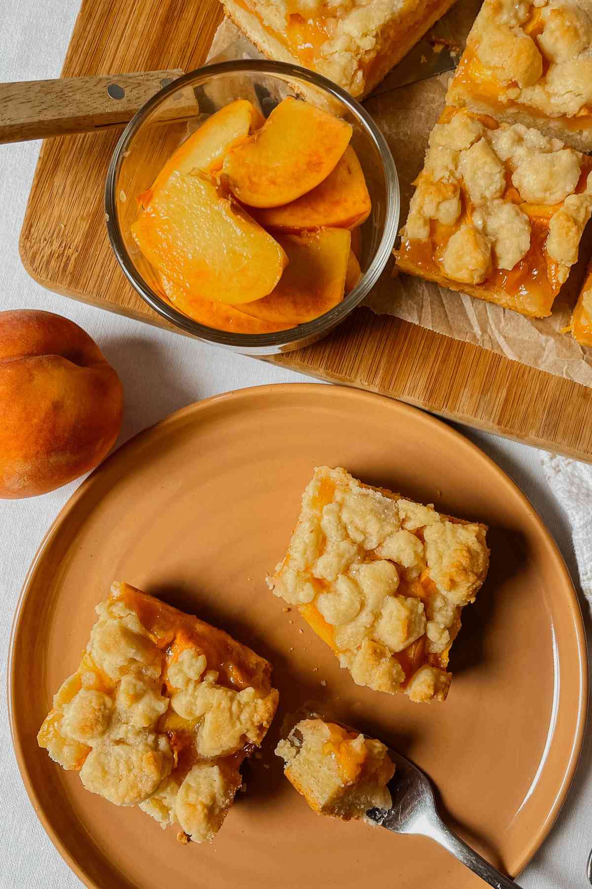 Sourdough peach crumb bar squares on orange plate with peaches in the background