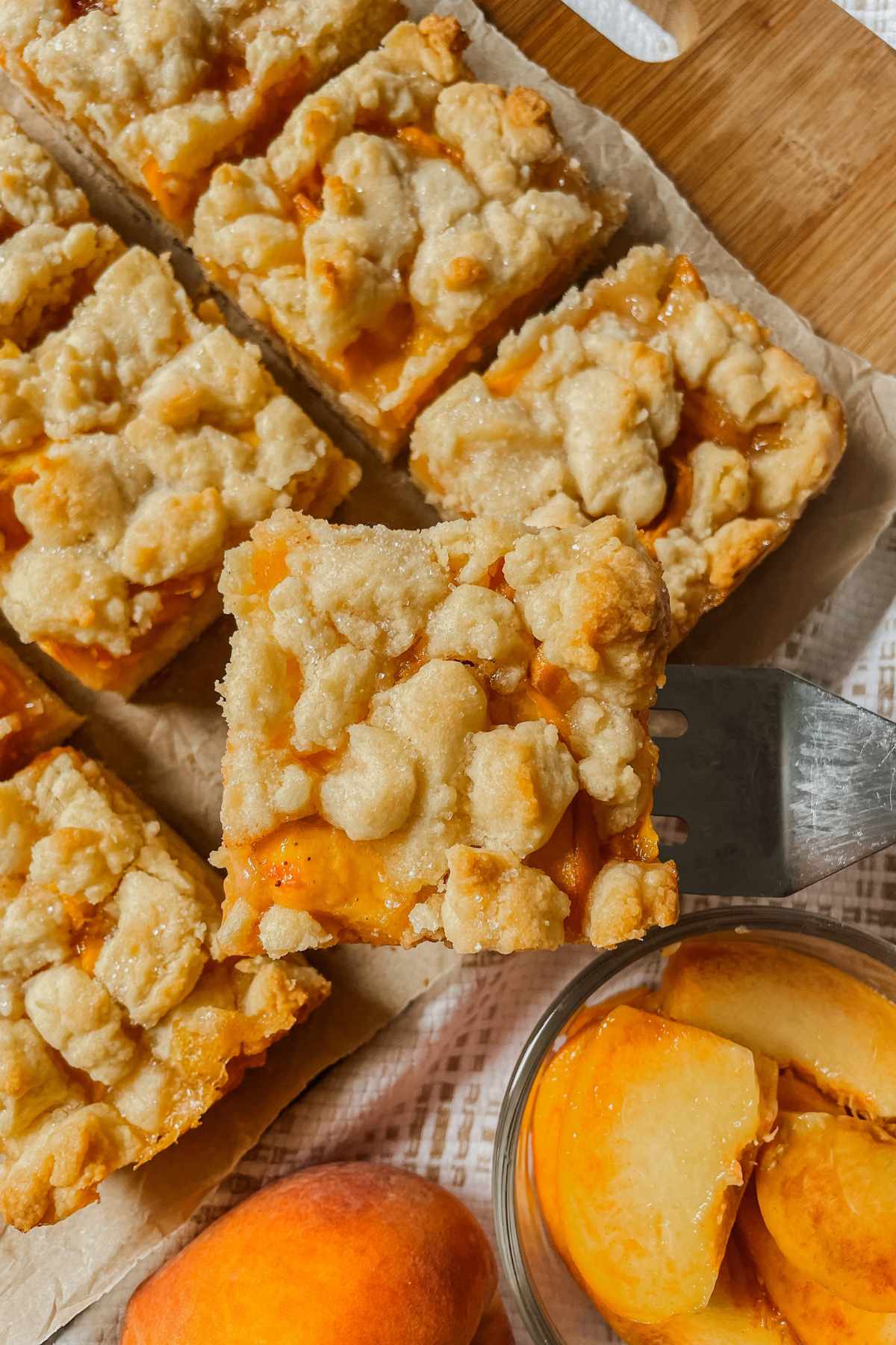 Sourdough peach crumb bar square held up on a square server with peaches in background