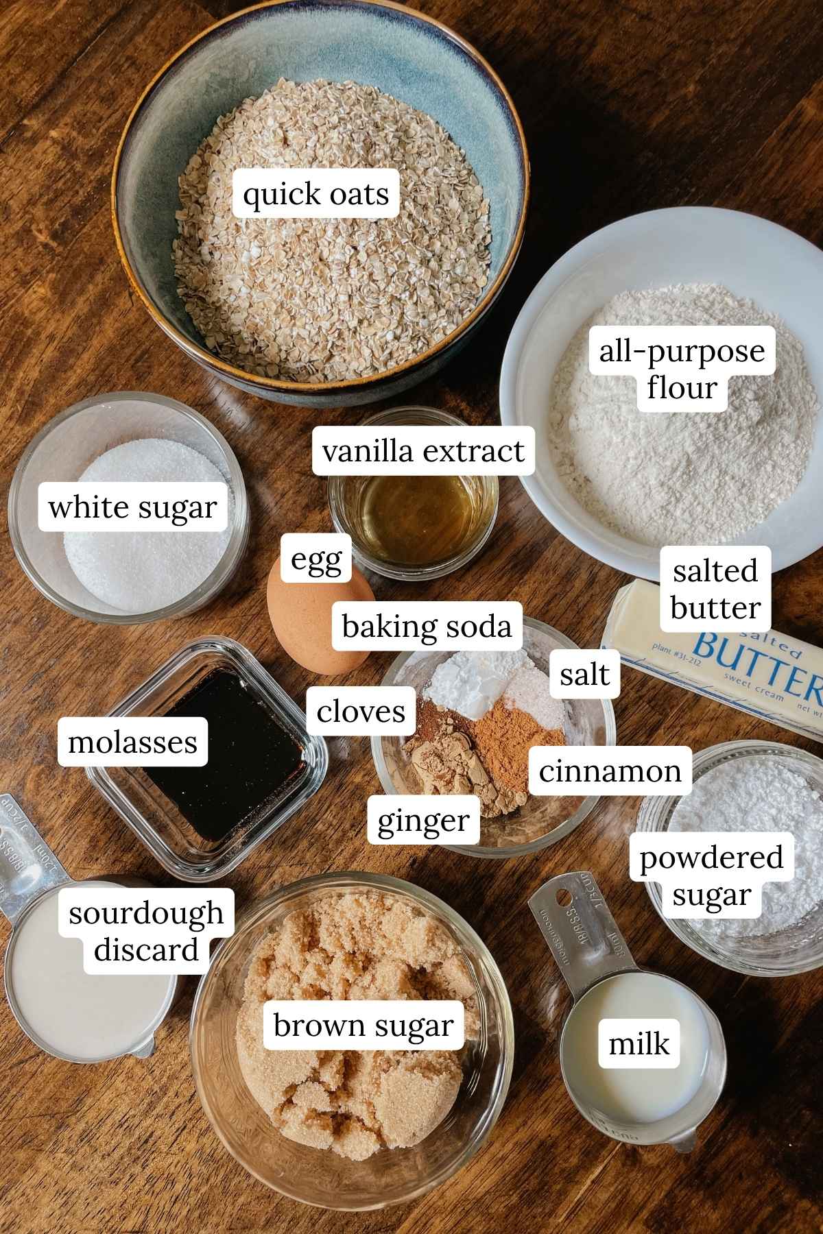 Ingredients for sourdough gingerbread iced oatmeal cookie bars labeled in bowls on a wooden table