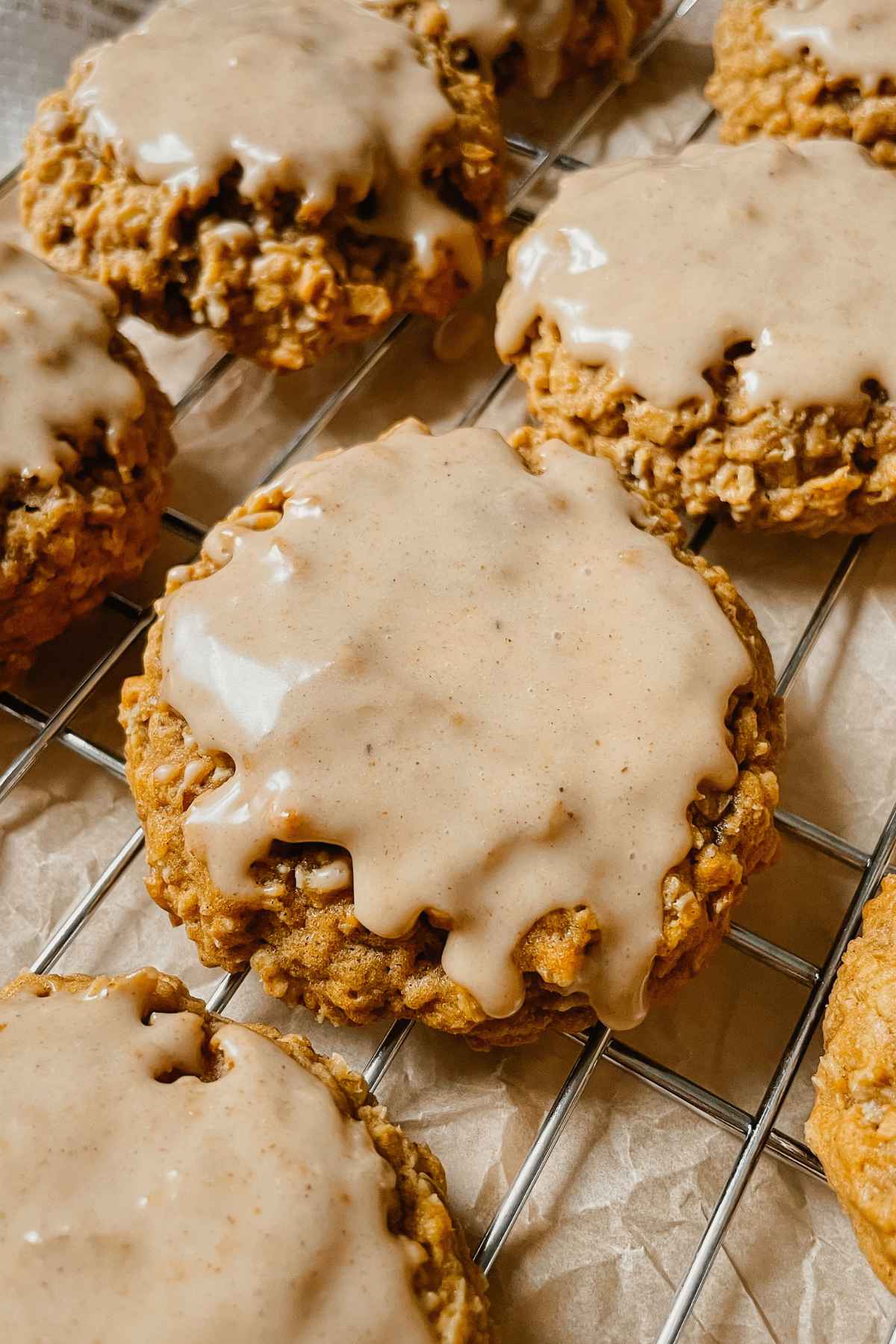 Close up of an iced sourdough pumpkin oatmeal cookie on wire cooling rack with brown parchment paper behind